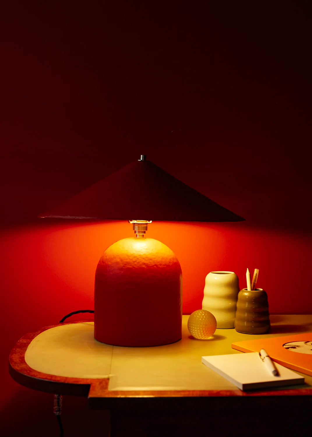 Desk with lamp and stationery against a dark red wall