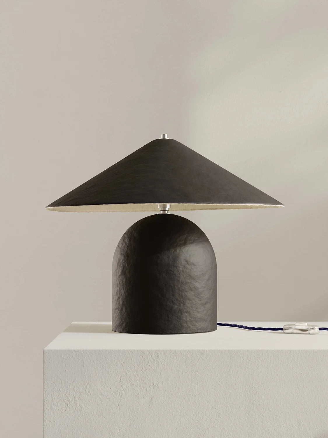 Brown-black table lamp on a white pedestal against a beige wall