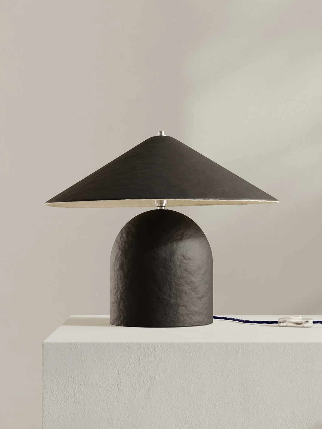 Brown-black table lamp on a white pedestal against a beige wall