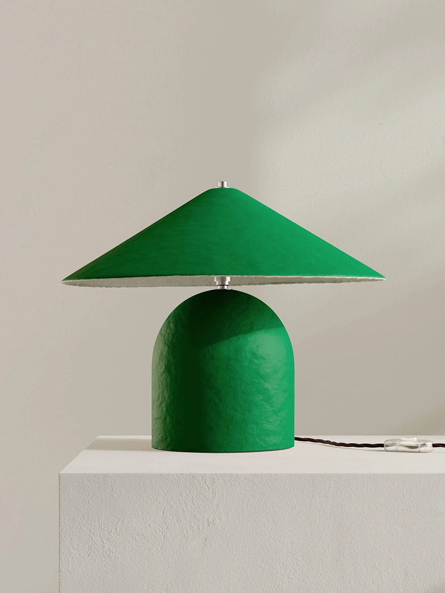 Green table lamp with a unique design on a white surface against a beige background