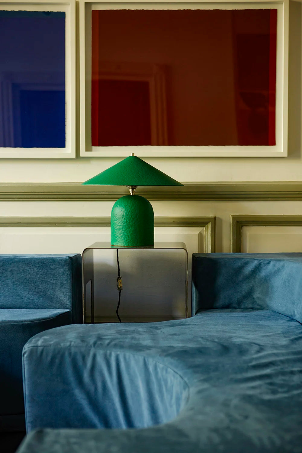 Green lamp on a side table beside a blue sofa with abstract art in the background
