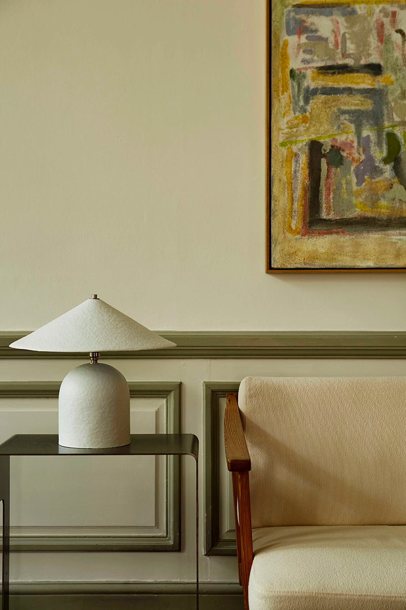 Lamp on a side table next to a beige armchair with abstract art on the wall.
