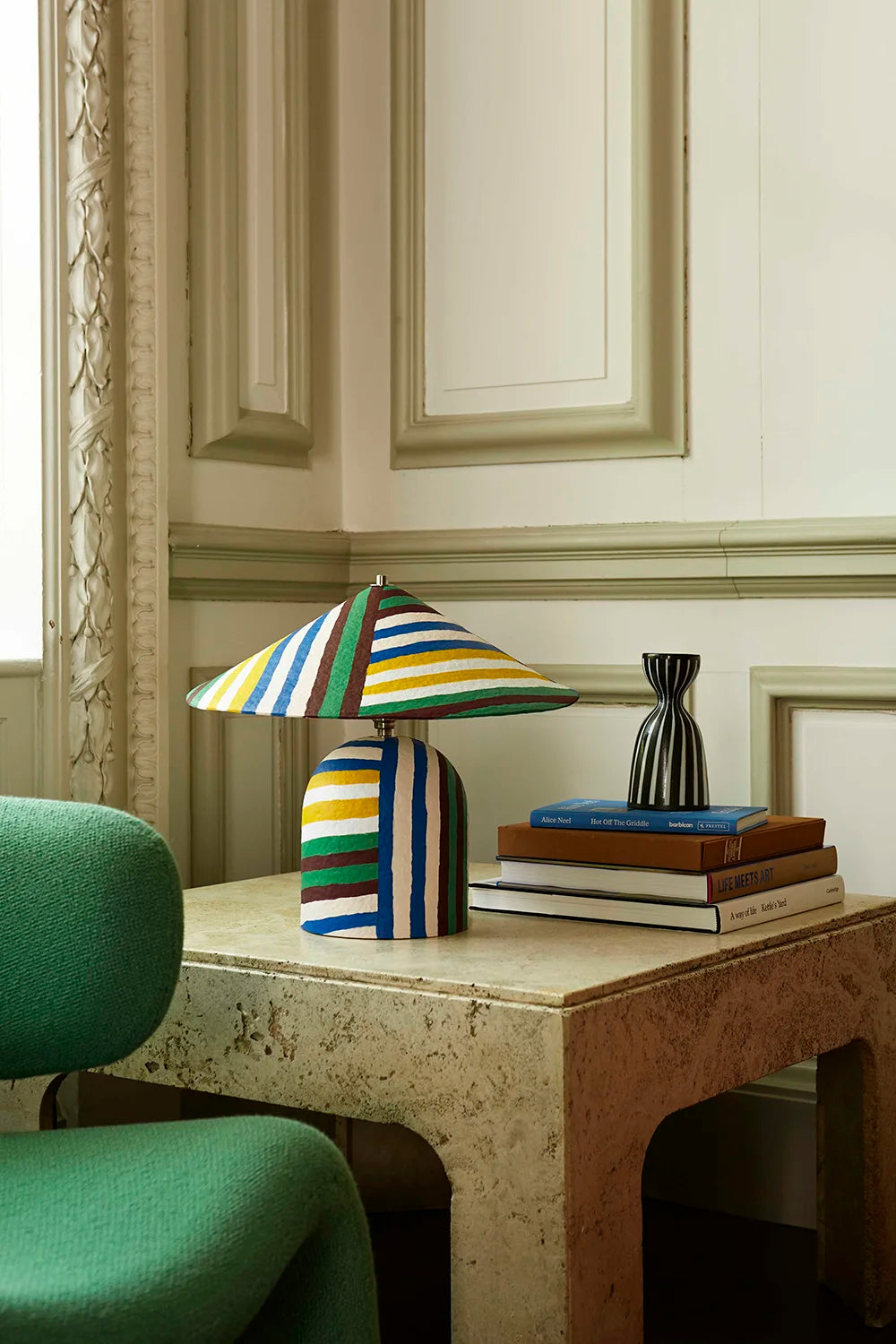 Colorful striped lamp on a table with books and decorative items in an elegant room.