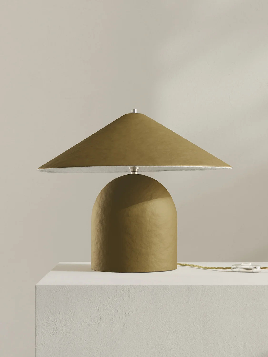 A modern table lamp with a textured moss-green dome base and a matching wide-brimmed cone shade, resting on a white pedestal against a neutral beige background.