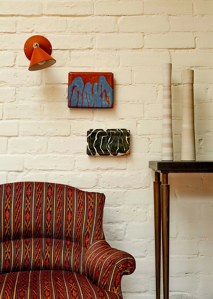 Decorative wall art and lamp on a white brick wall with a patterned chair in the foreground.