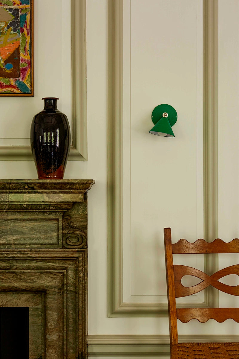 Decorative elements in a room with a vase on a mantelpiece, a green wall lamp, and a wooden chair.