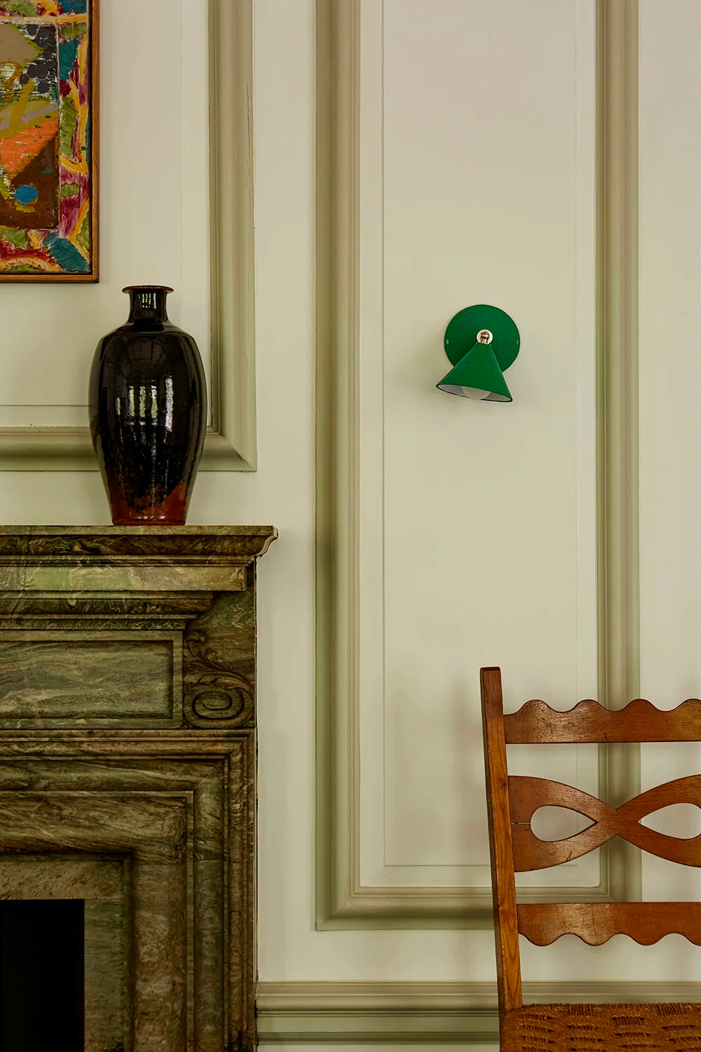 Decorative elements in a room with a vase on a mantelpiece, a green wall sconce, and a wooden chair.