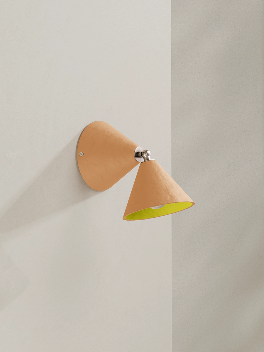 Wall-mounted lamp with a peach shade and yellow interior on a light gray wall.
