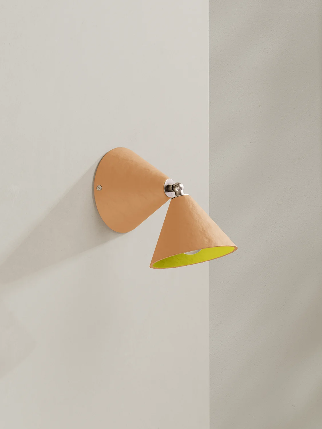 Wall-mounted lamp with a peach-coloured shade and yellow interior on a light gray wall.