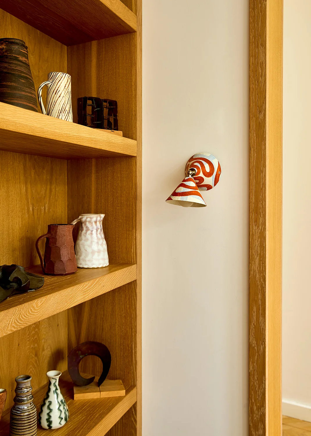 Wooden shelf with decorative items and a wall-mounted light fixture featuring a swirly pattern.