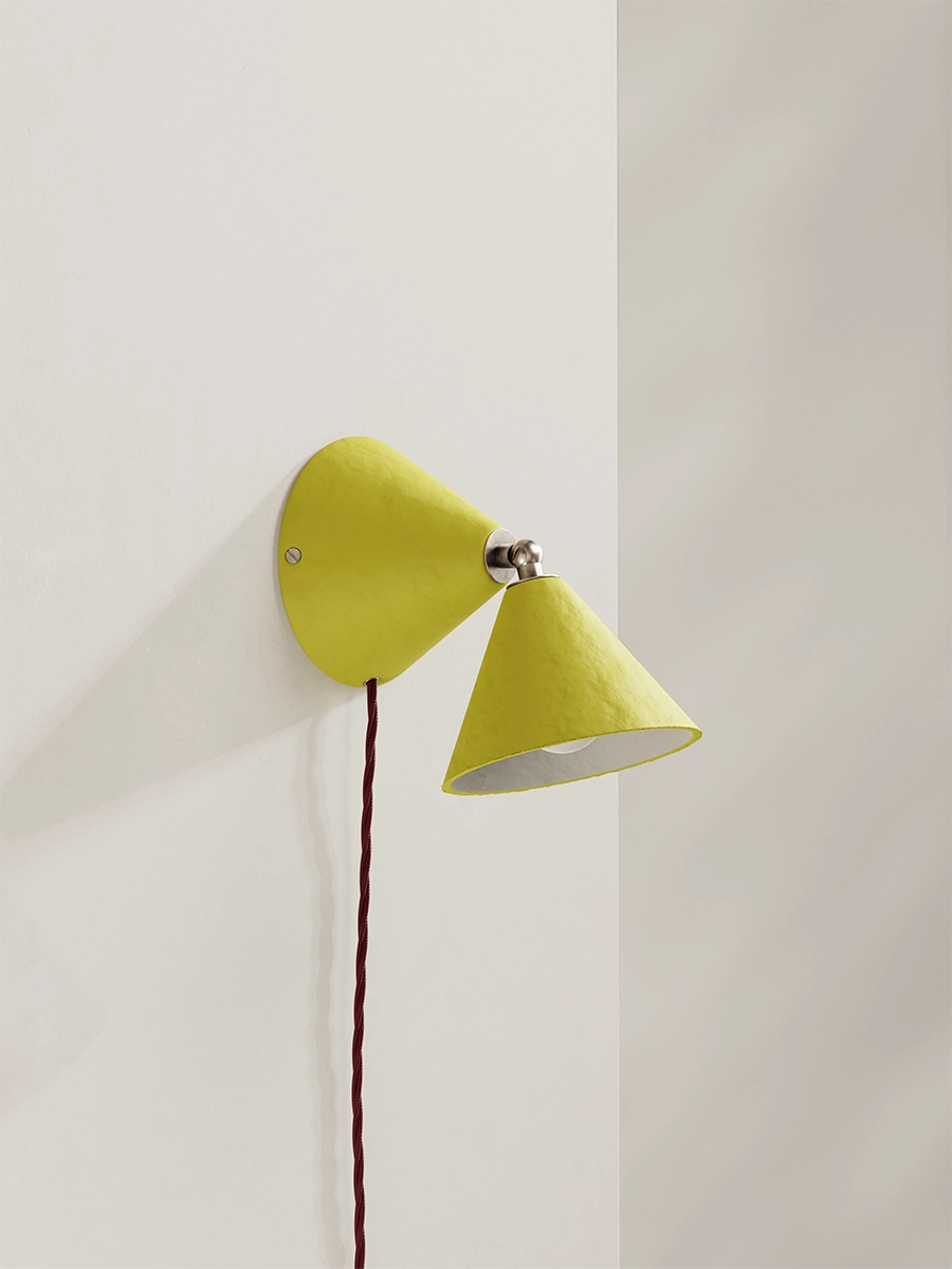A citrus-yellow wall lamp with burgundy flex against a plain wall