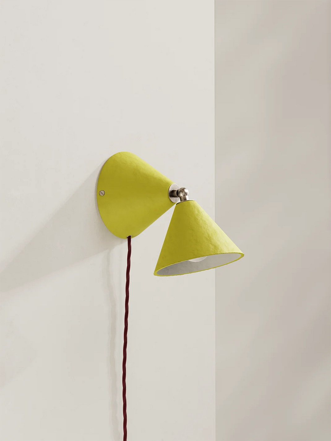 Yellow wall lamp with a burgundy cord on a light gray background