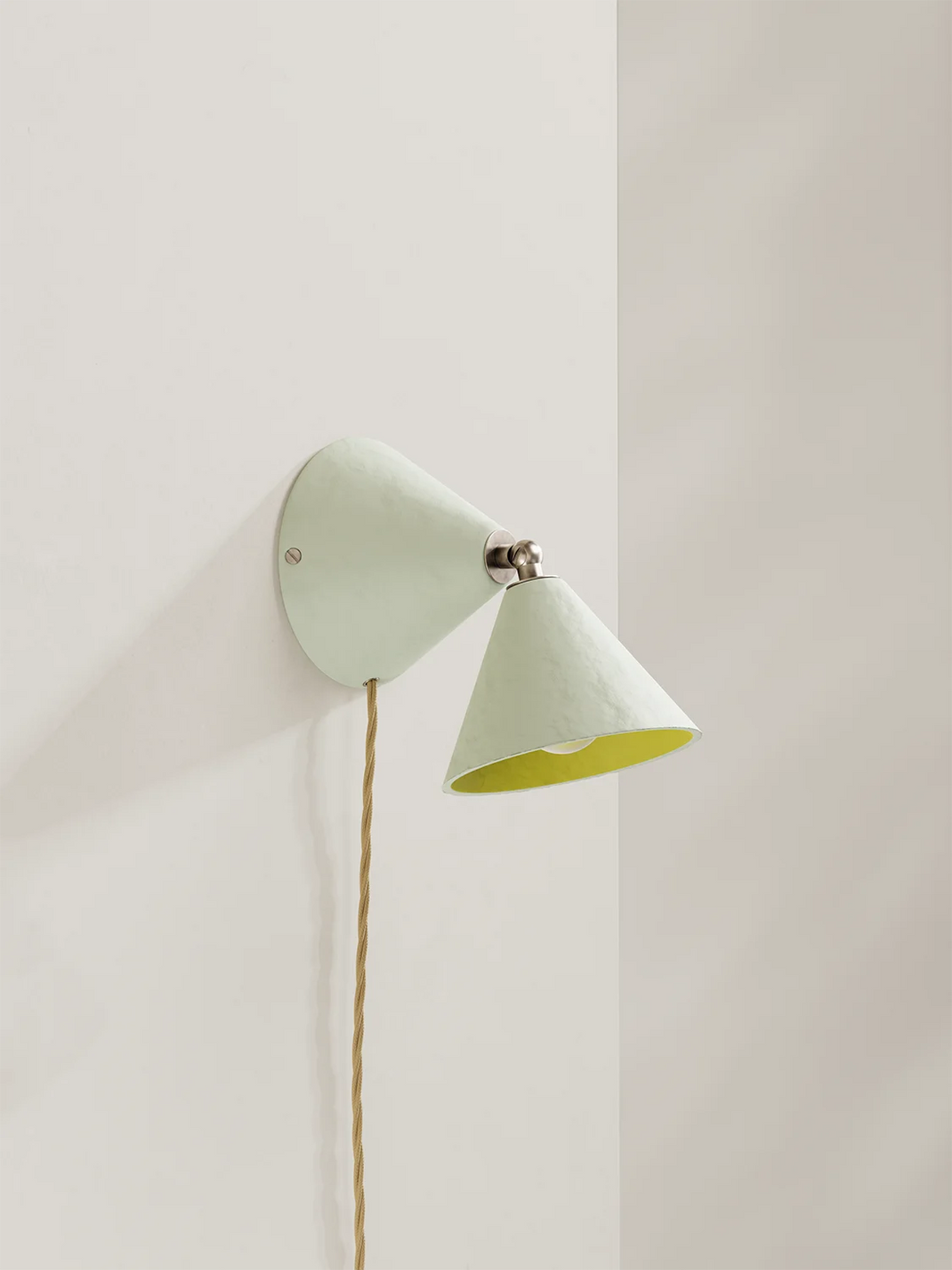 A modern wall sconce with an off-white outer shade and a bright yellow inner shade, mounted on a warm off-white wall with a visible cord.