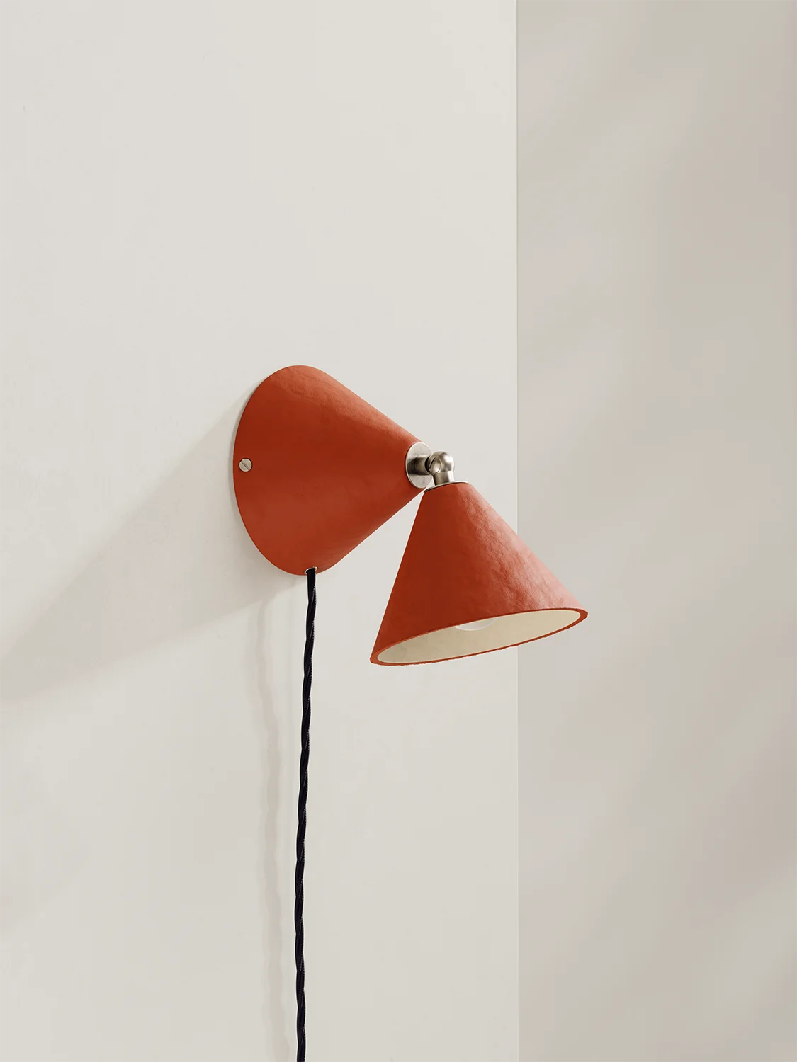 A modern cone-shaped wall sconce in terracotta orange with a dark blue cord, mounted on a clean white wall.