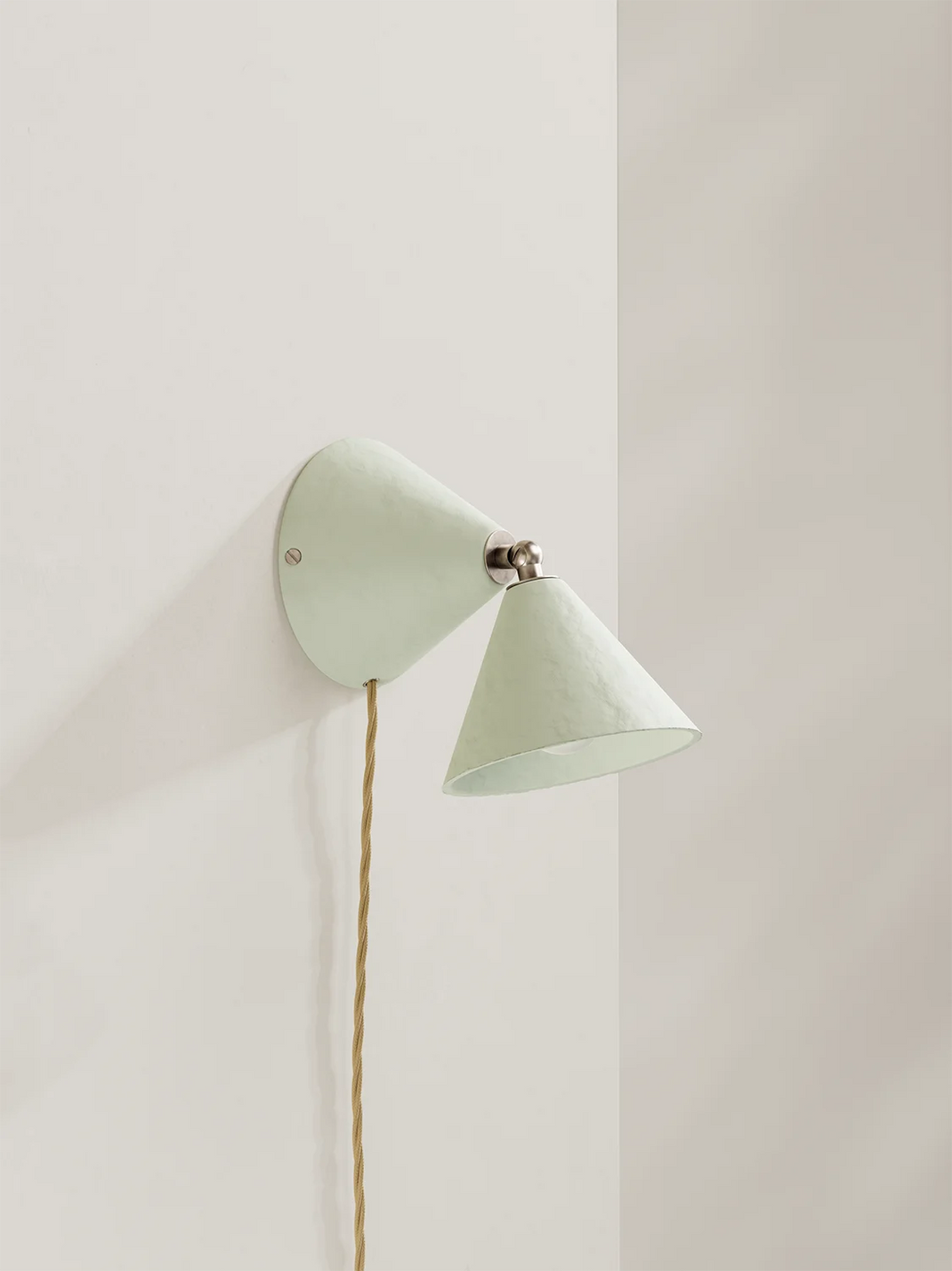 An off-white wall lamp with a cone-shaped shade on a white wall.
