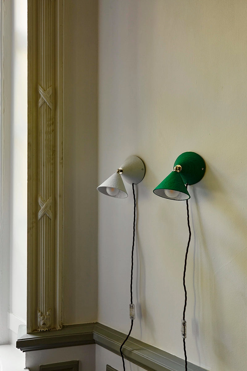 One white and one green wall lamp side by side on a wall