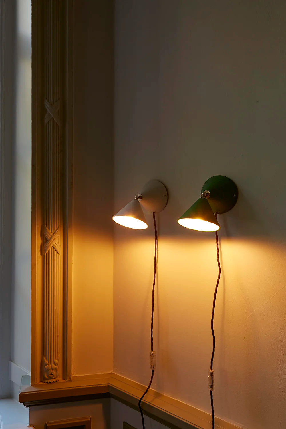 Two wall-mounted lights on a white wall with a decorative cornice.