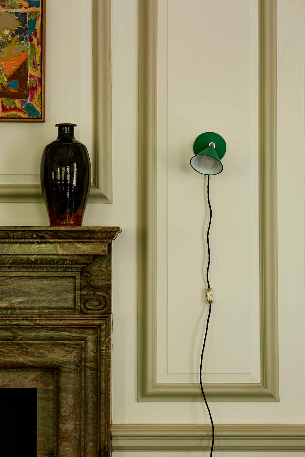 Wall-mounted lamp with a green shade next to a fireplace in a room with decorative wall art.