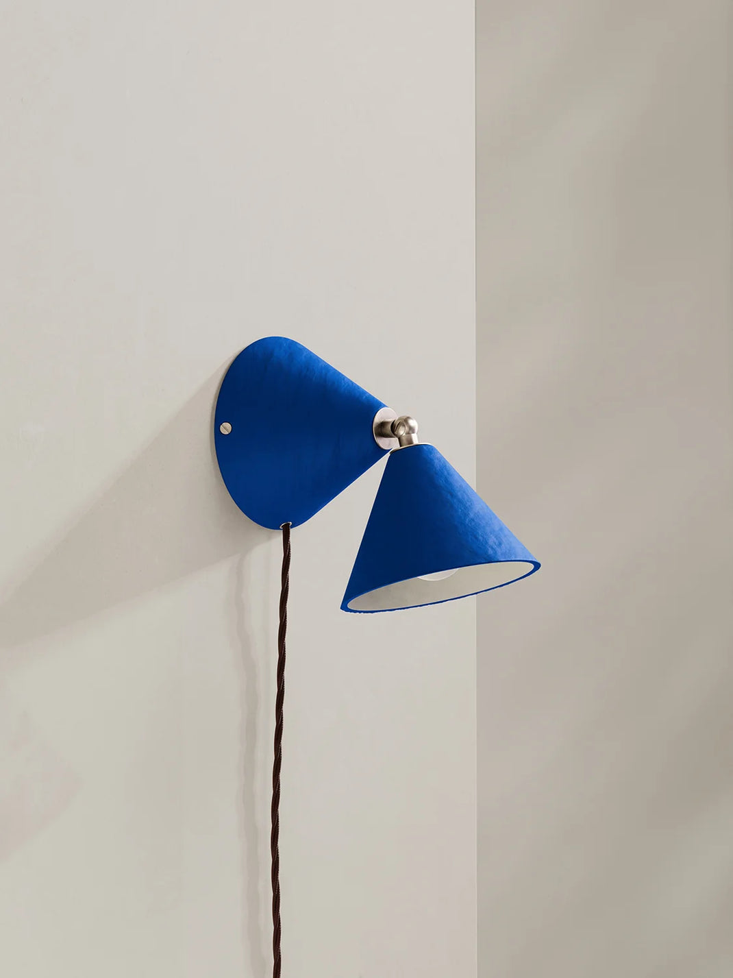 A modern blue wall sconce with two cone-shaped shades, mounted on a light beige wall.