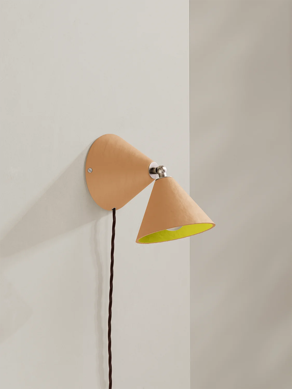 Wall-mounted lamp with a peach exterior and yellow interior on a light gray wall.