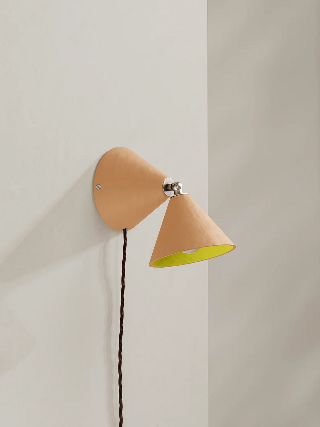 Wall-mounted lamp with a peach exterior and yellow interior on a light gray wall.