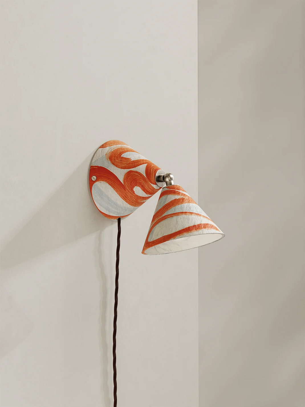 Wall-mounted lamp with orange and white swirl shade on a neutral background