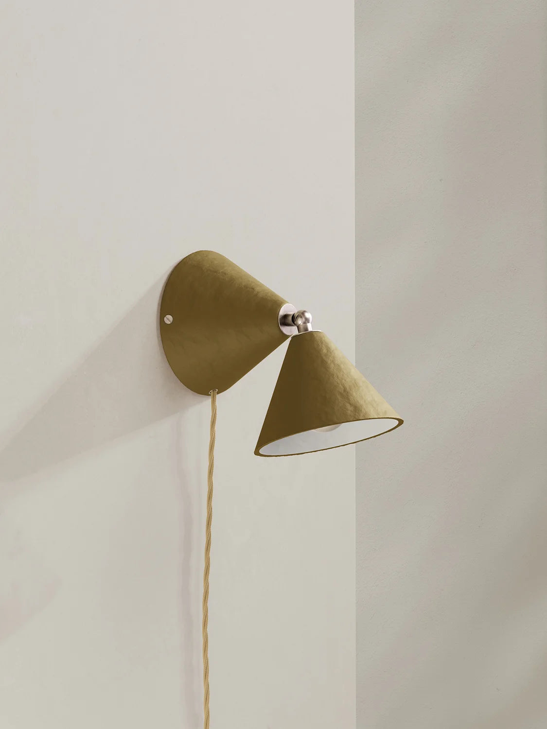 A modern wall-mounted cone-shaped sconce in a textured olive green finish with a silver metal accent and a hanging cord, shown against a minimalist off-white wall.