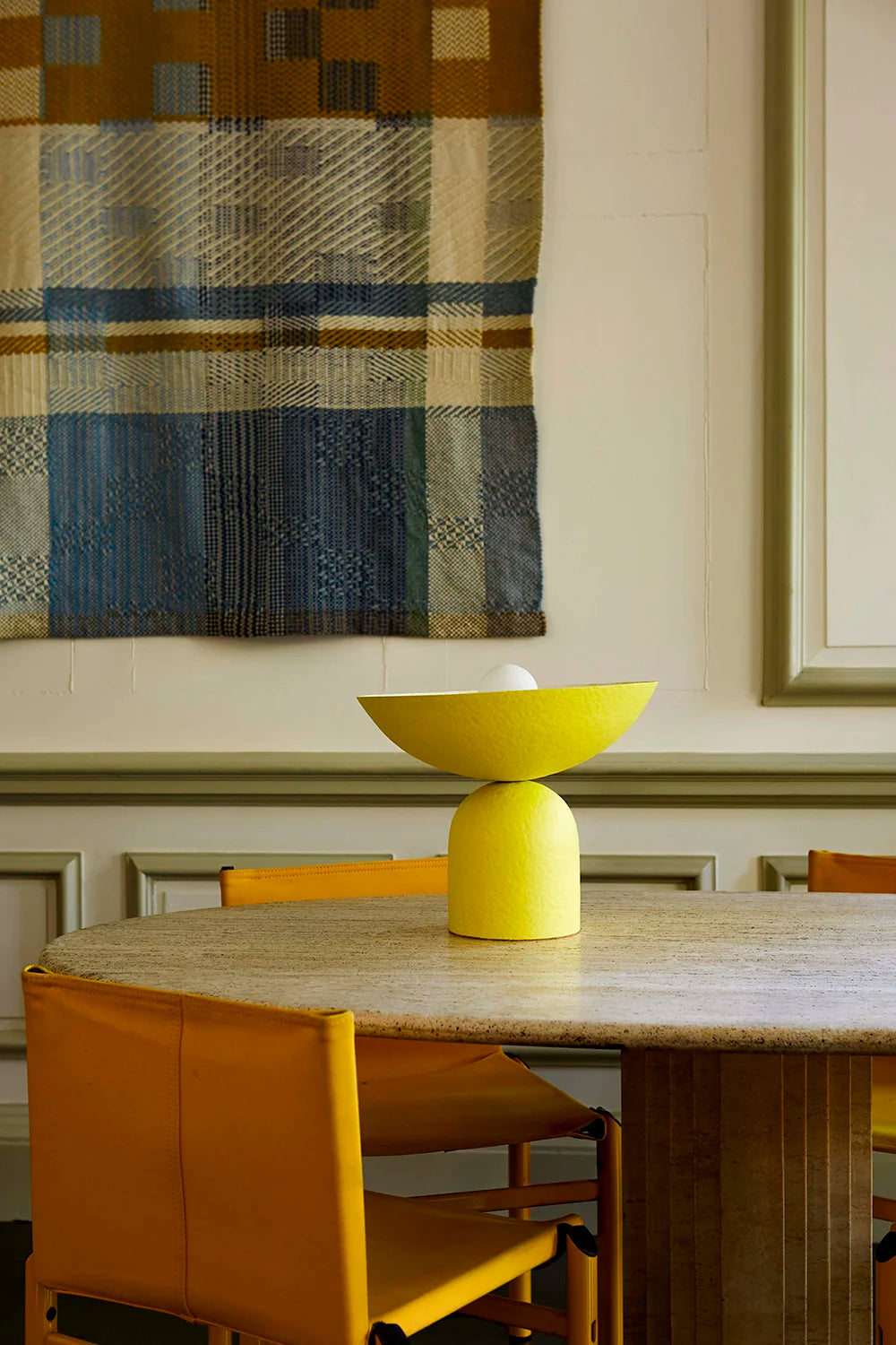 Dining room with a plaid wall hanging, yellow chairs, and a vibrant yellow table lamp.