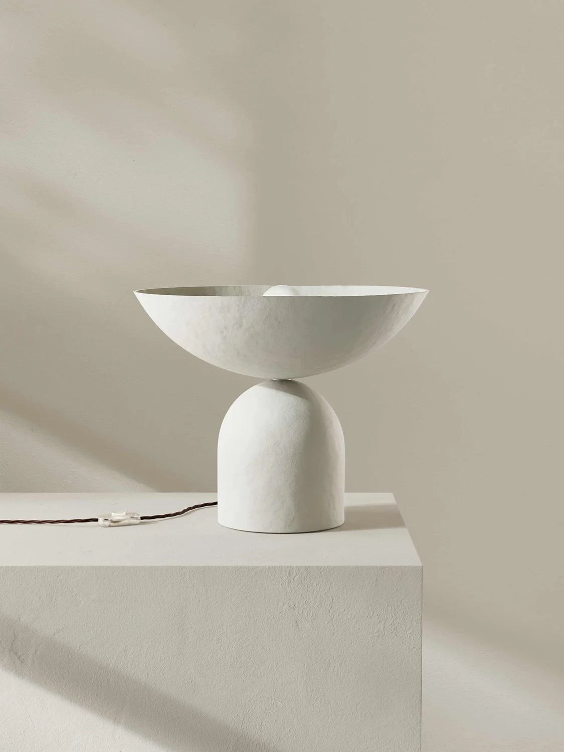 Minimalist white lamp on a light gray pedestal against a beige background