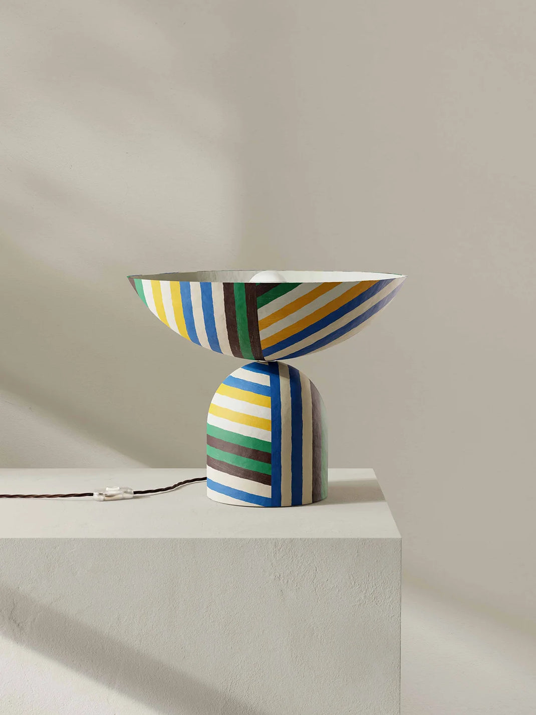 Colorful striped table lamp on a white pedestal against a beige background