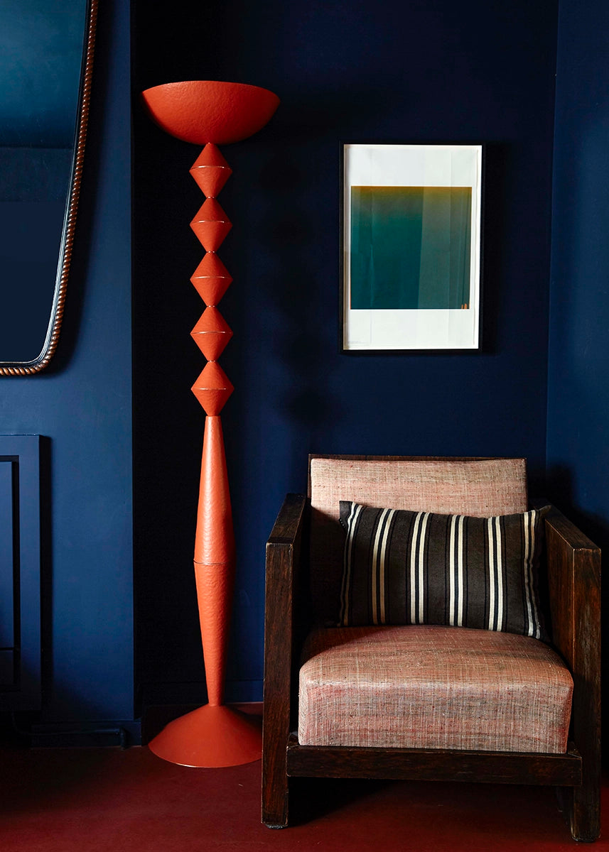 Geometric floor lamp in orange against a dark blue wall