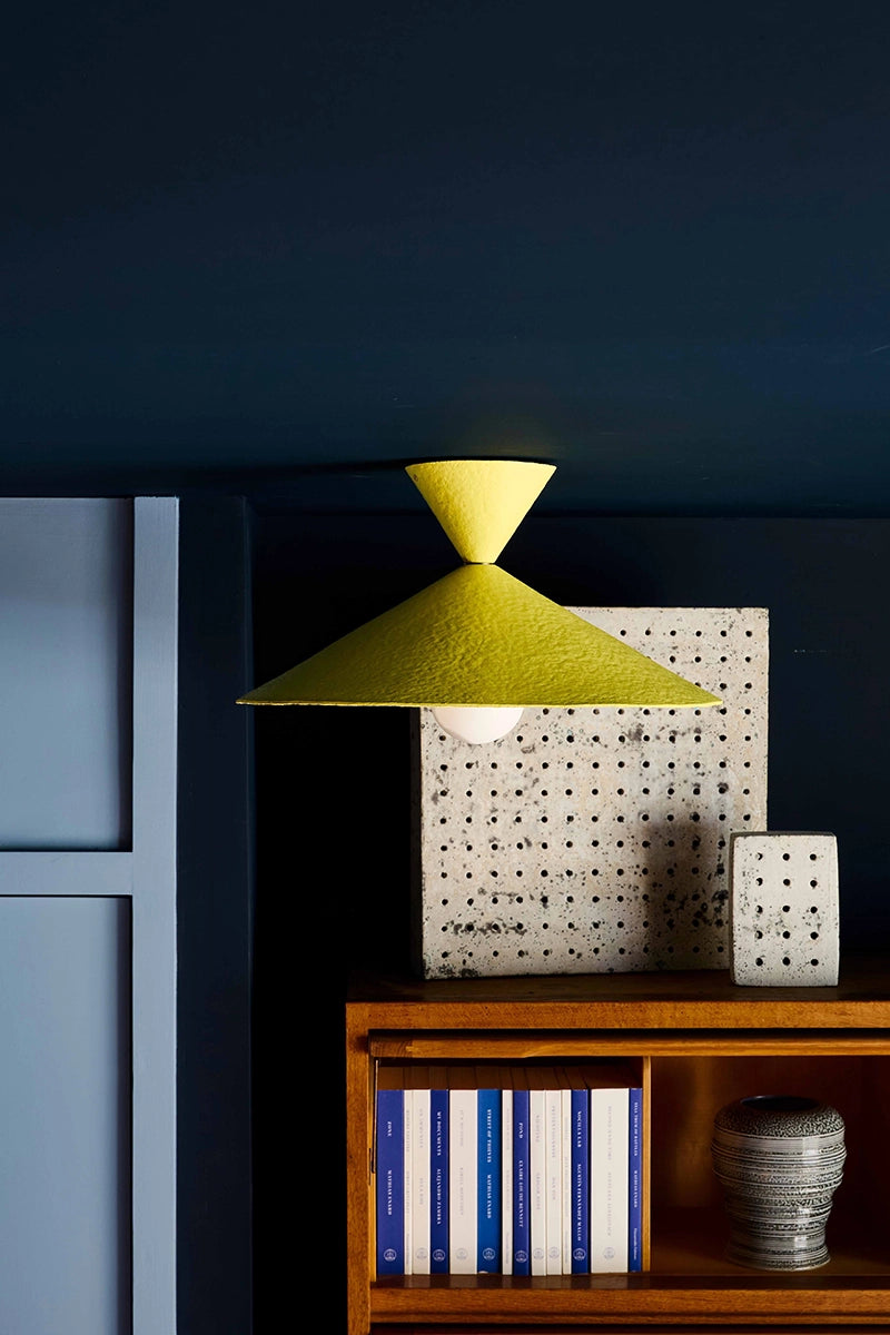 Yellow lampshade above a wooden shelf with decorative items against a dark wall.