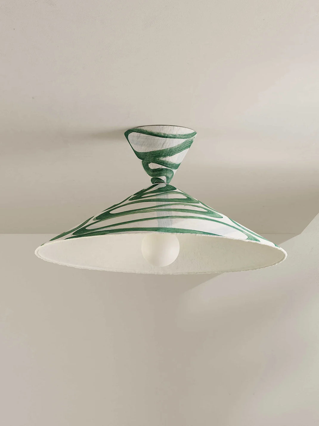 A ceiling-mounted light fixture with a wide cone shade and a matching top cap, decorated with green hand-painted swirls, shown against a plain off-white wall and ceiling.
