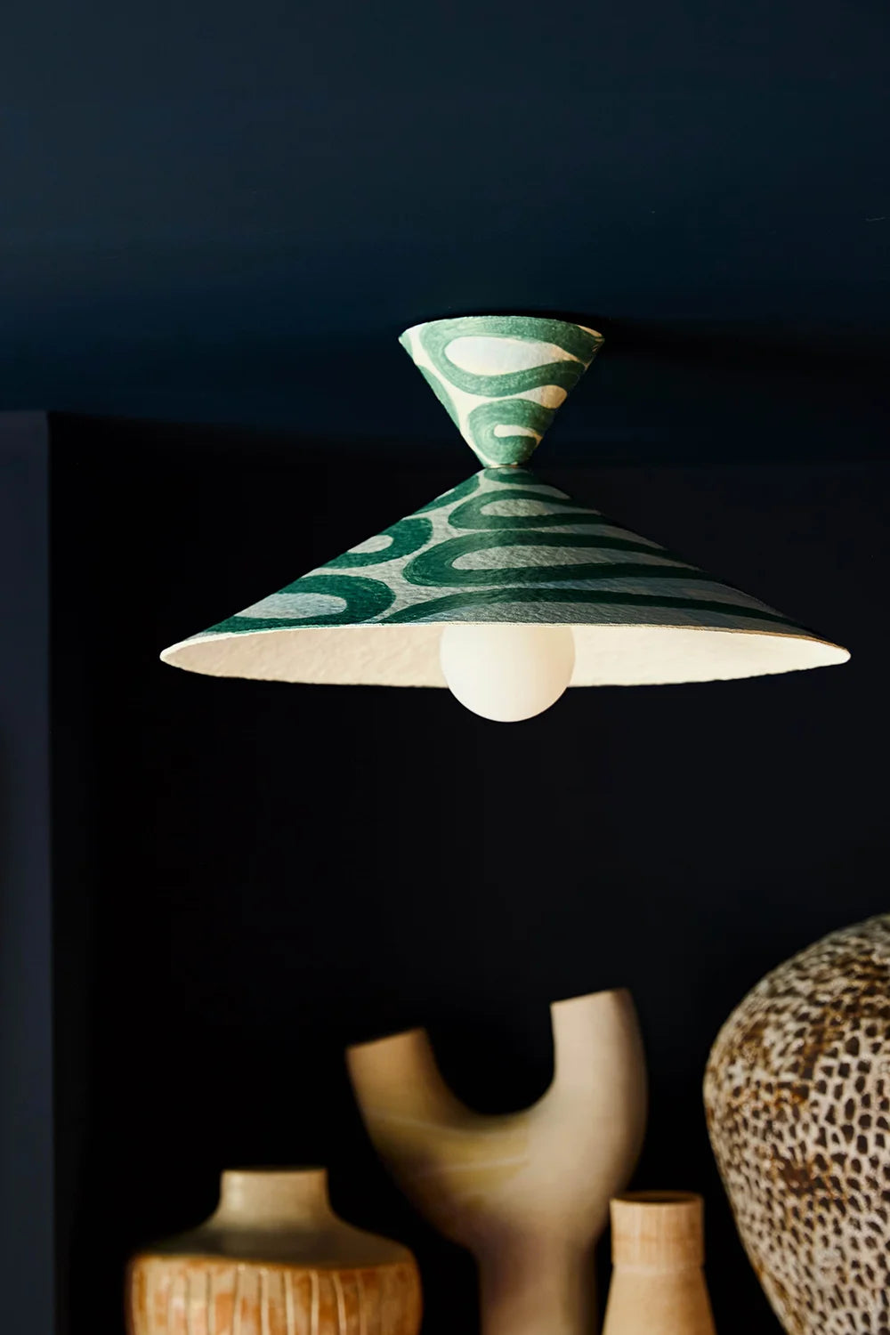 Ceiling light fixture with green patterned shade against a dark background