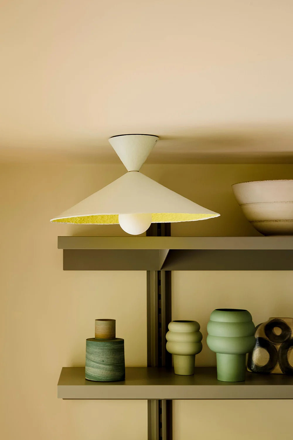 Modern lamp with a white shade in front of a shelf and beige wall