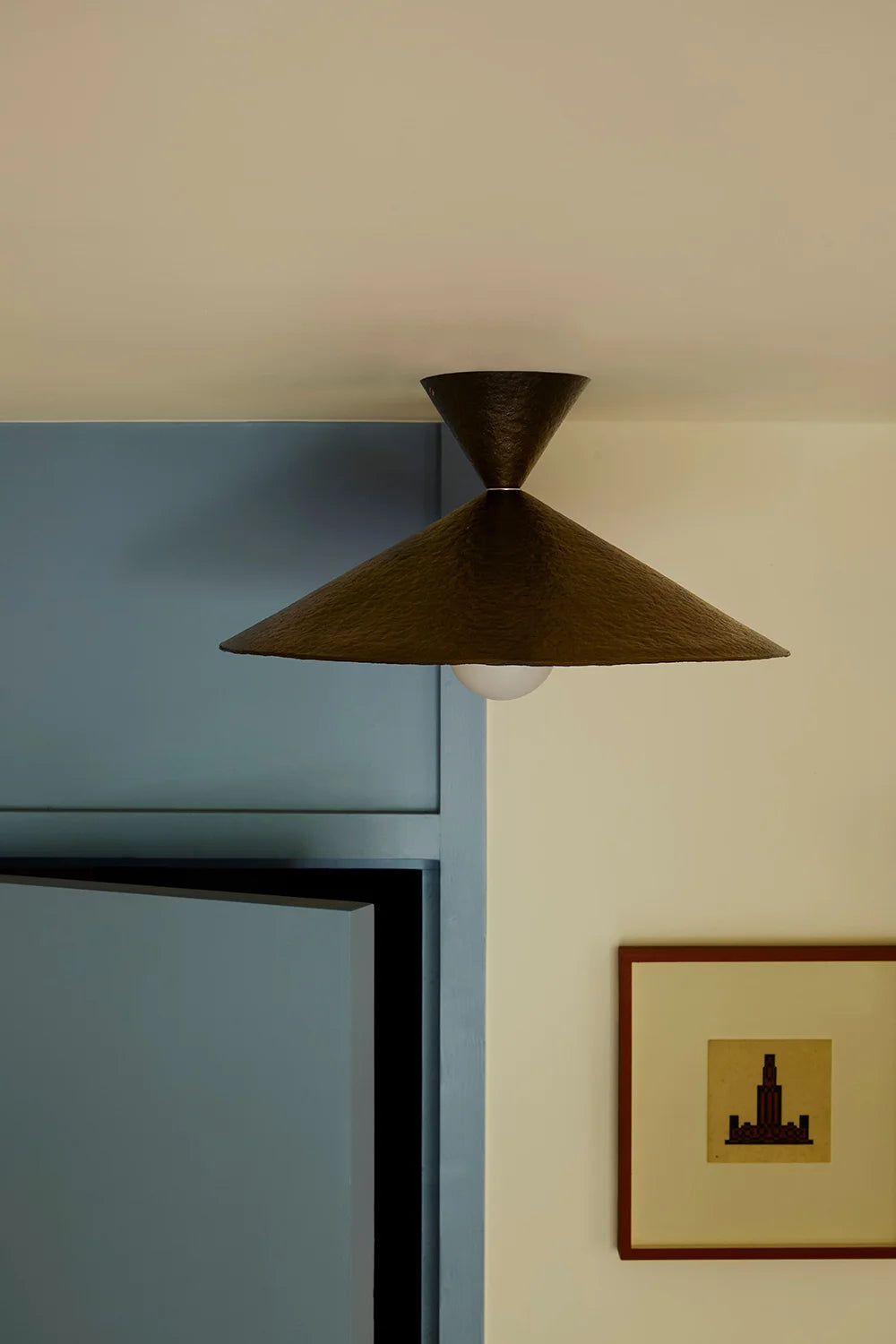 Modern pendant light hanging in a room with a blue door and framed picture.