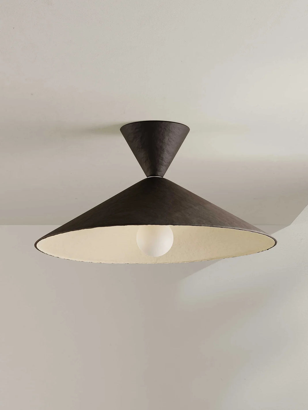 A modern flush mount ceiling light fixture with a dark brown exterior and a wide, shallow conical shade featuring a warm cream-colored interior. A single white bulb is visible inside the shade, set against a neutral off-white ceiling.